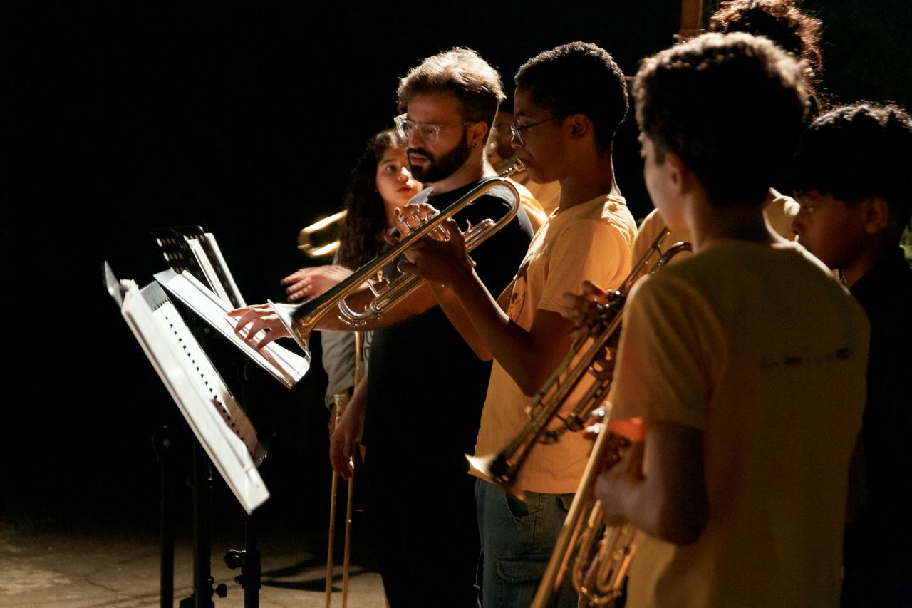 A Favela Brass teacher demonstrating trumpet technique to young students at an evening rehearsal