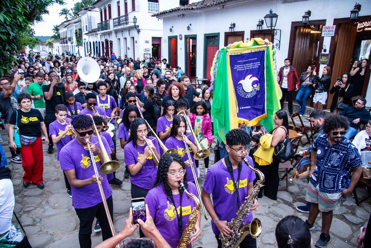 Favela Brass students in purple shirts playing saxophones and trombones as they parade through the streets of Paraty